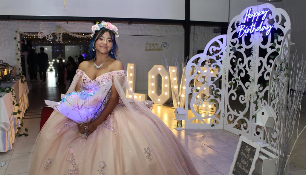 Quinceañera feliz en su fiesta con vestido rosa y ramo iluminado, rodeada de una hermosa decoración.