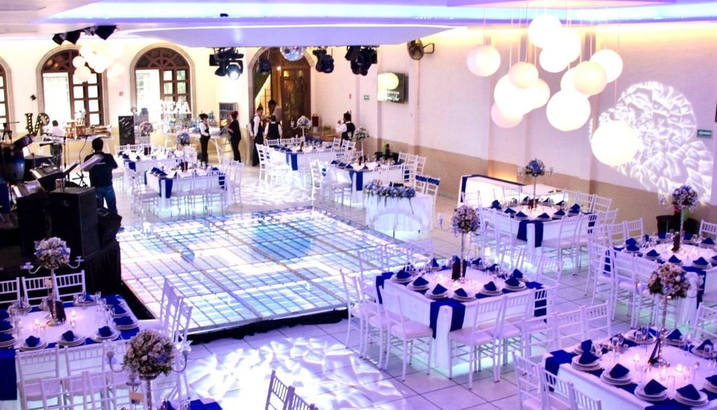 "Evento nocturno con mesas decoradas en tonos oscuros, luces y ambiente elegante.