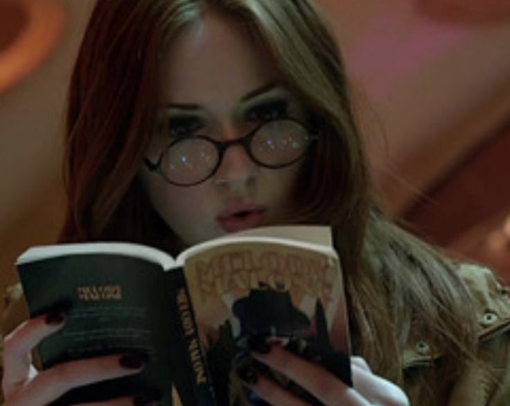 a woman in glasses and a jacket is reading a book