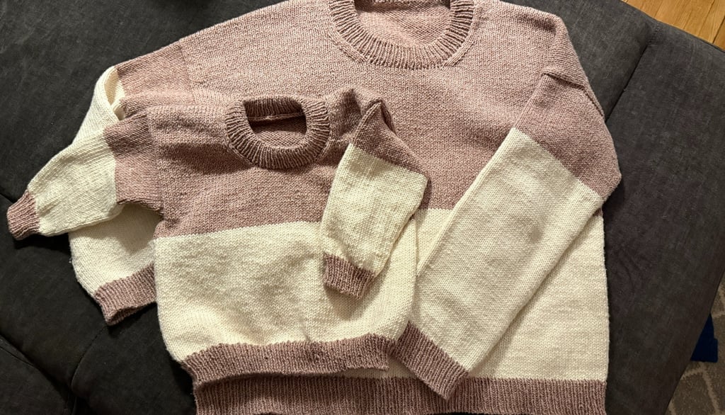 Hand-knitted matching adult and child color-block sweaters in dusty rose and cream wool yarn.