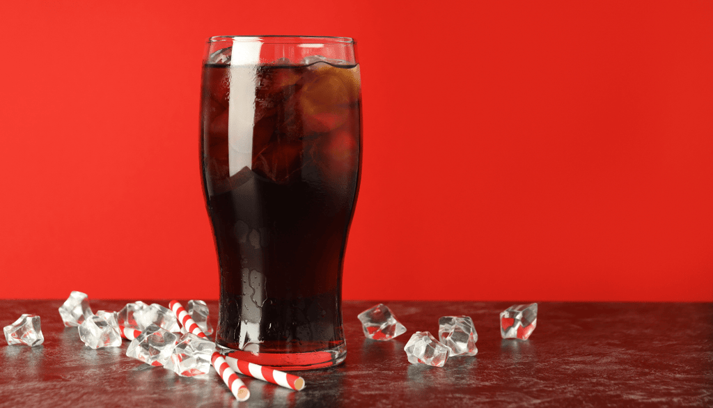 Glass of dark cola with ice cubes and striped paper straws on a red background — concept image relat