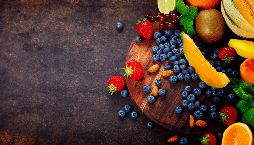 Eine bunte Auswahl an frischem Obst mit Heidelbeeren, Erdbeeren, Melone und Mandeln auf einem runden Holzbrett