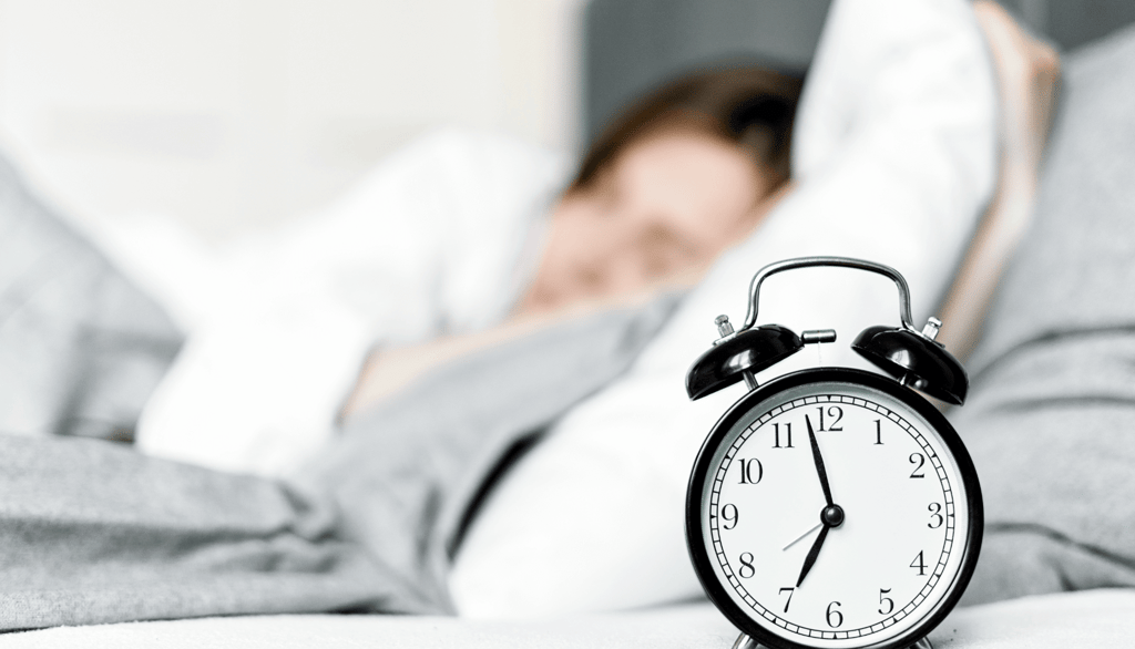 a person laying in bed with a clock on the side of the bed