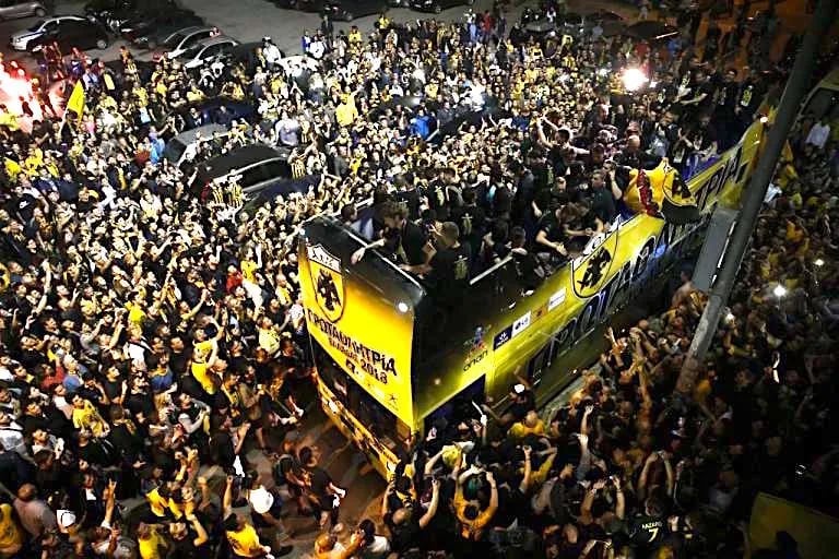 AEK Athen Fan im Stadion jubelt leidenschaftlich während eines Spiels, Fahnen wehend, Gesänge schallend, in voller Fan-Ausrüs
