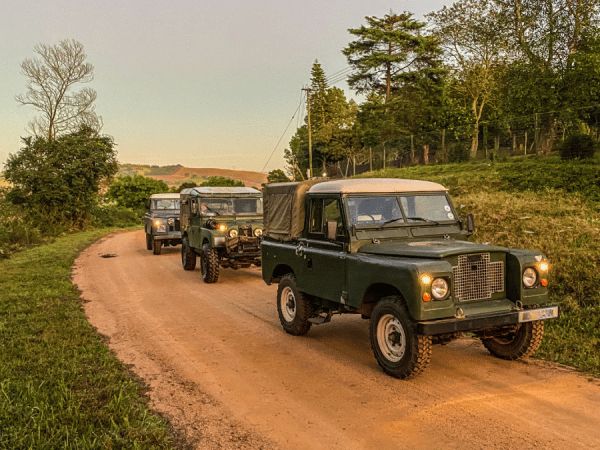 a group of three classic land rovers driving down a dirt road
