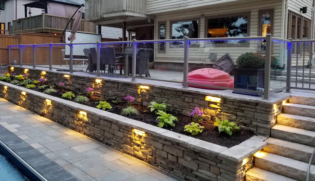 Modern stone retaining wall with integrated LED garden lighting and a glass deck railing.