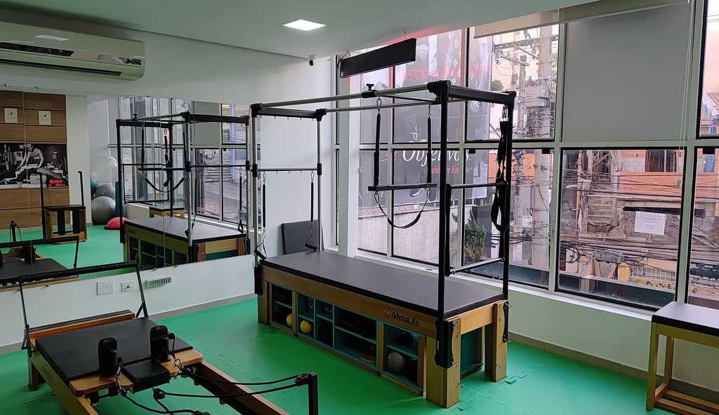 Professional Pilates Cadillac trapeze table in a bright studio with large windows and wall mirrors.