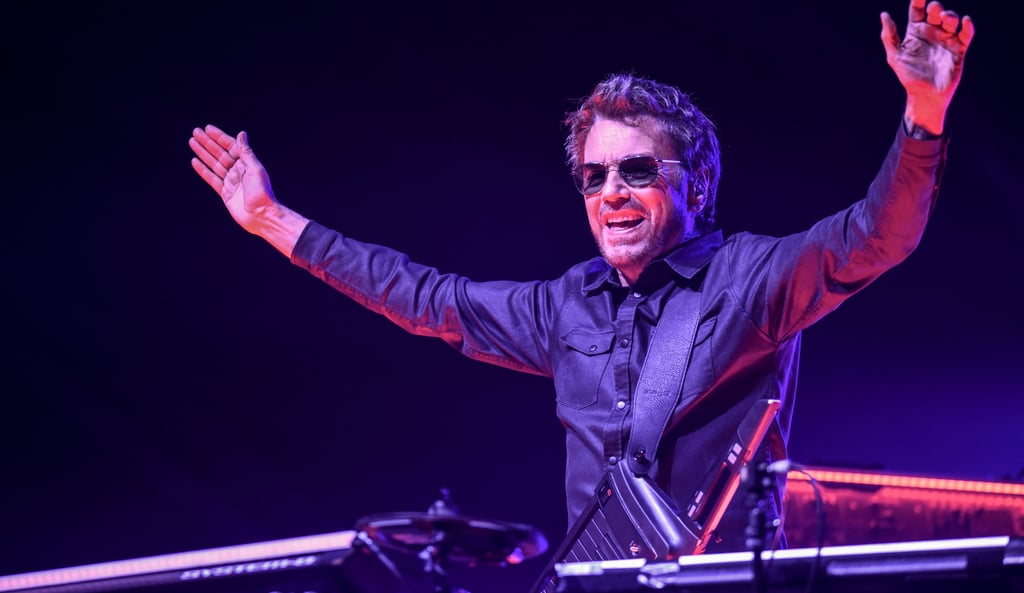 Jean-Michel Jarre euphorically performing live on stage during an electronic music concert.