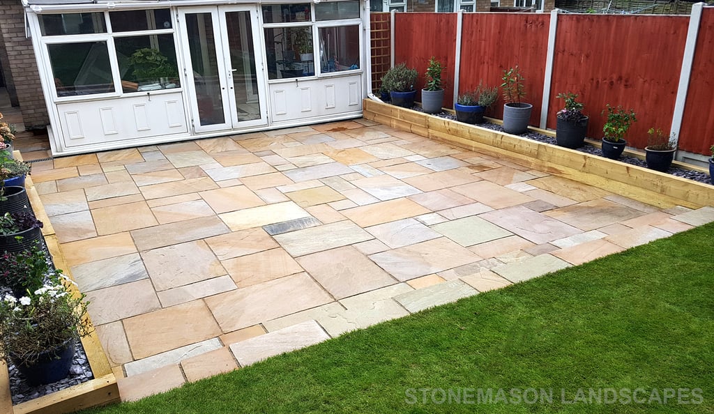 Large sandstone patio and raised wooden sleeper planters