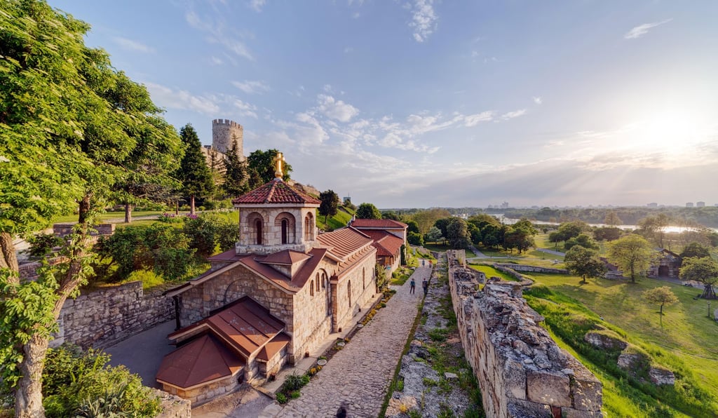 The Ruzica Church and stone walls of Belgrade Fortress overlooking the Sava river at sunset.