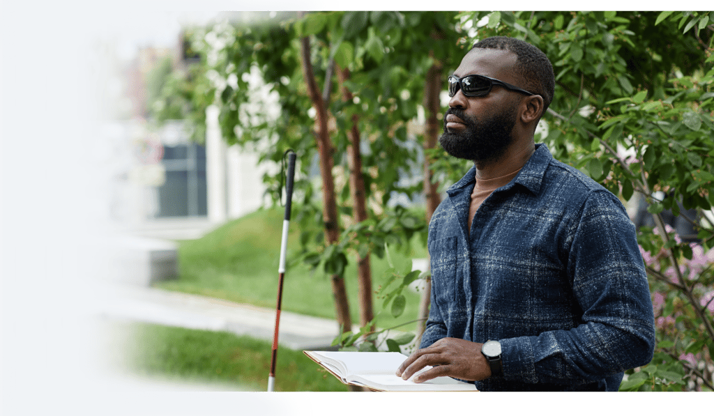 Man reading a Braille book in the park with his cane, highlighting accessible reading for the blind