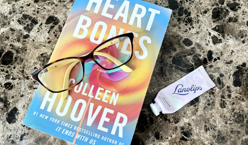 Lanolips lip balm on a nightstand beside a book and reading glasses ready for a nightly routine