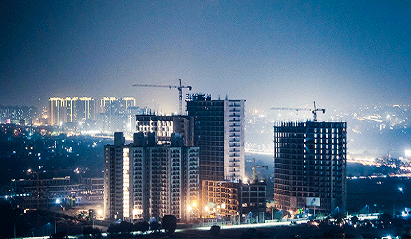 A city skyline at night featuring illuminated skyscrapers and buildings against a dark sky.