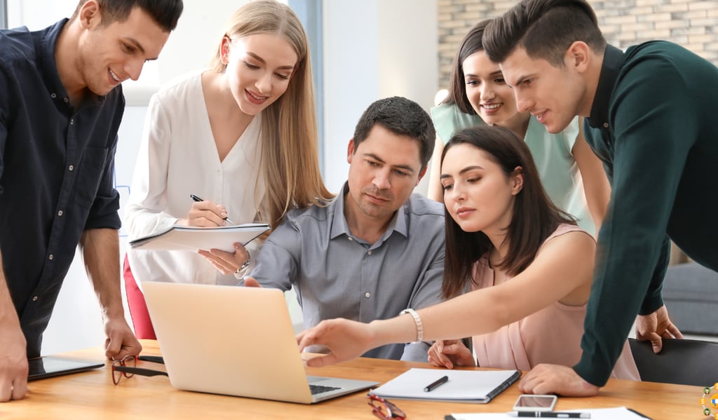 a group of people standing around a laptop computer