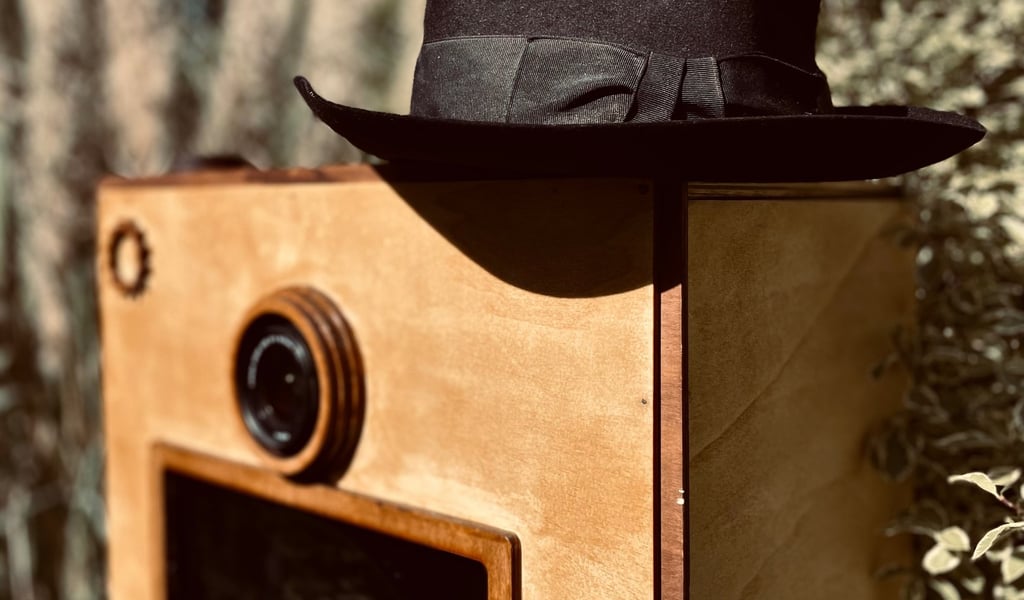 Détail du photobooth en bois vintage avec objectif apparent et chapeau posé, mise en scène poétique 