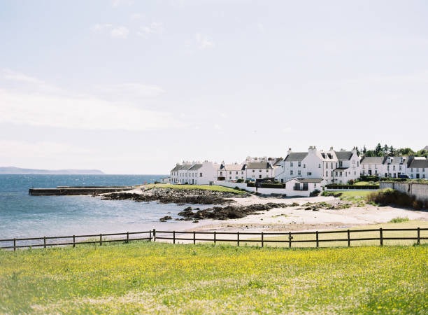 White coastal houses overlooking a sandy beach and rocky shoreline in a scenic Scottish village.