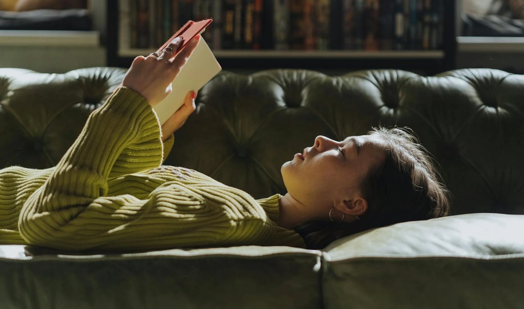 Uma jovem tranquilamente em um sofá, lendo um livro de artes visuais.