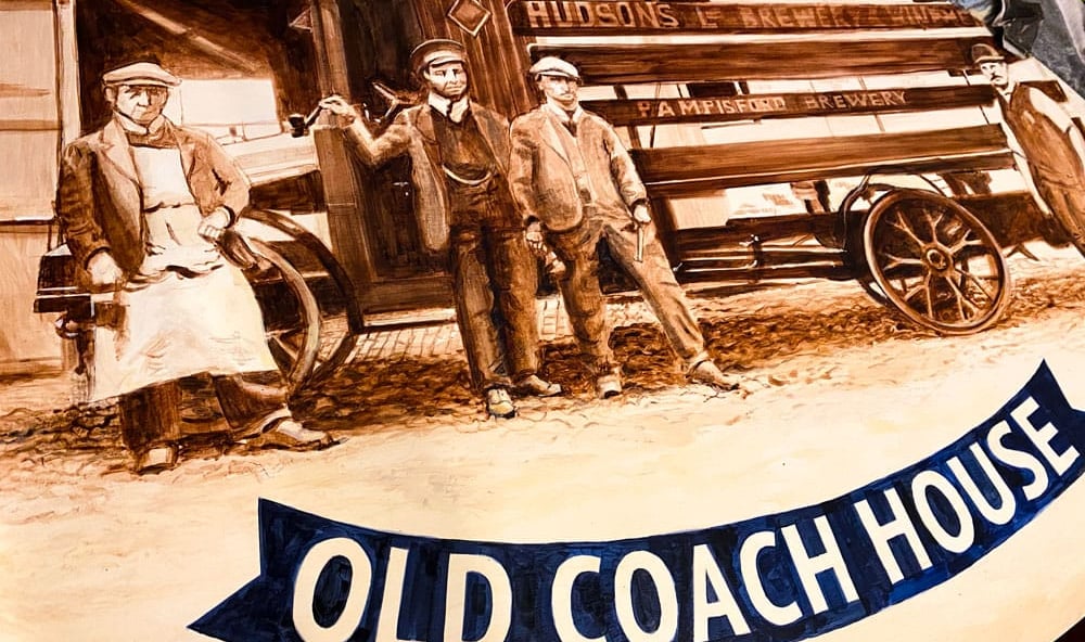 Close-up of angled pub sign with painted brewery staff