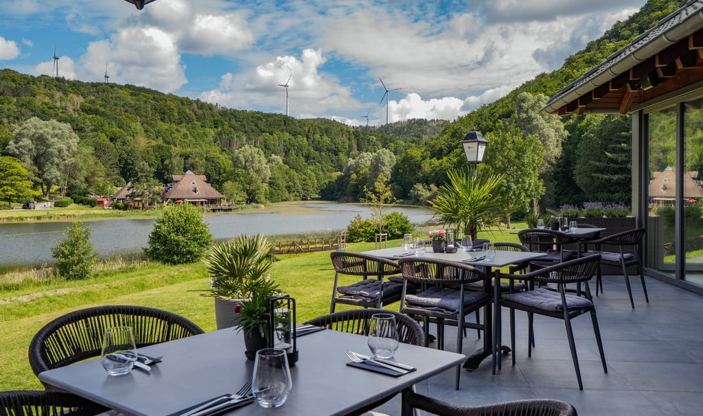 „Außenterrasse eines Seerestaurants mit Blick auf grüne Hügel und einen ruhigen See