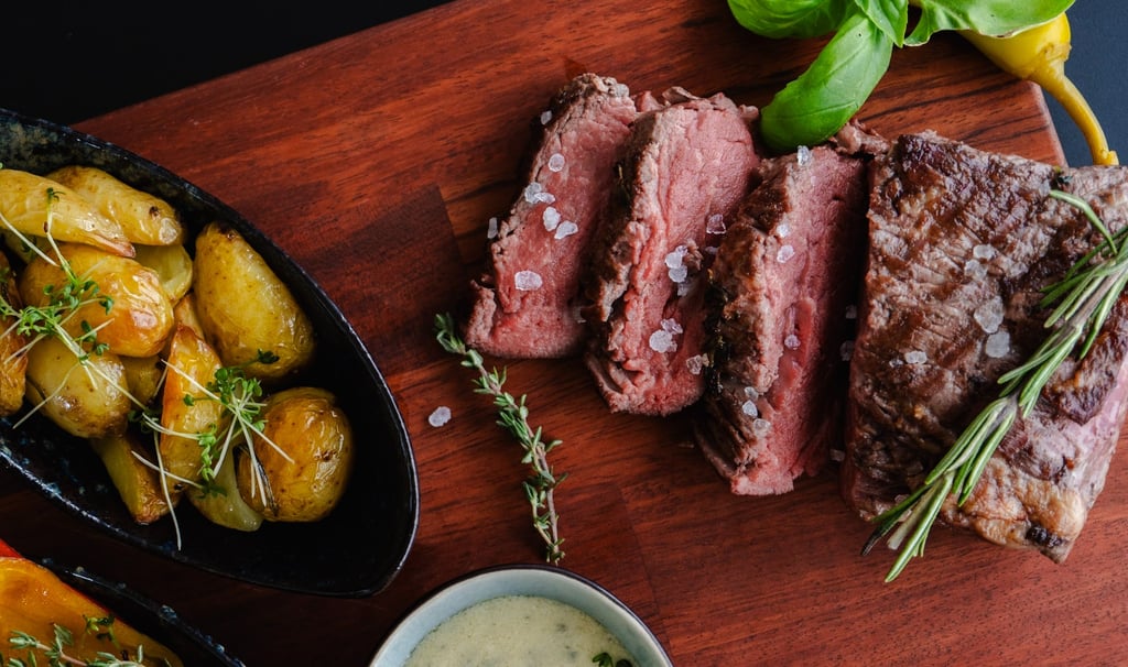 Saftig aufgeschnittenes Rindersteak (Medium) mit Meersalz und Rosmarin auf Holzbrett neben Röstkarto