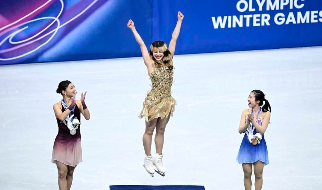 Alysa Liu jumping with both arms overhead on Olympic podium