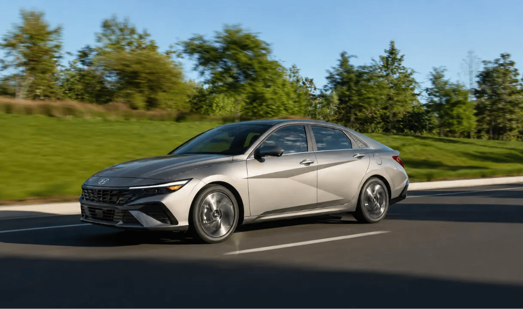 Hyundai Elantra 2026 prata em movimento em rodovia com paisagem arborizada ao fundo.