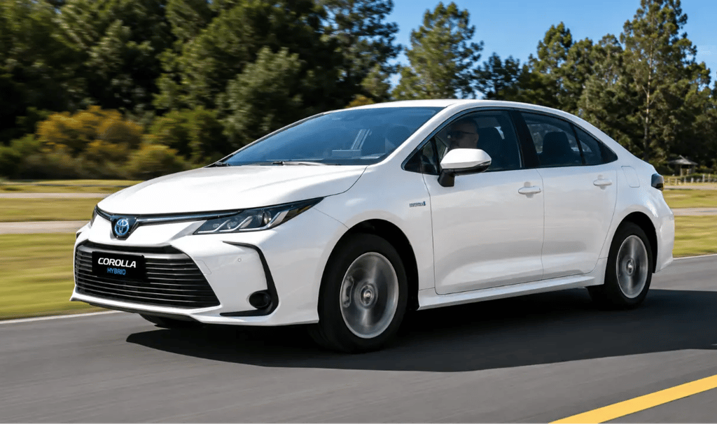 Toyota Corolla Hybrid branco em movimento por uma rodovia cercada por árvores