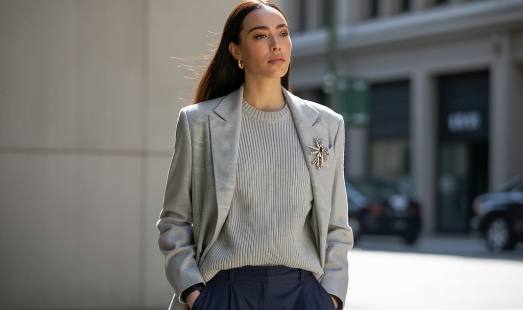 Woman wearing a grey blazer, ribbed knit sweater, and star brooch in a street style fashion shot.