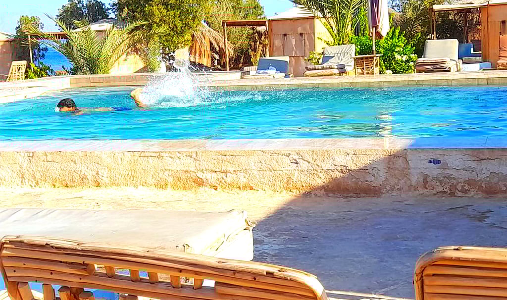 Gutt som svømmer i bassenget nær sjøen og bungalow på beduinstjernen Egypt