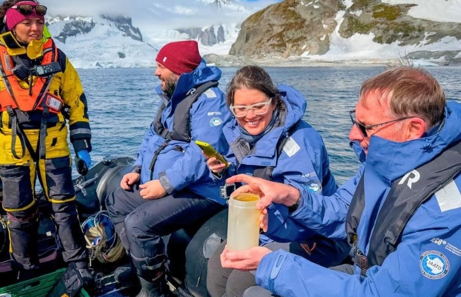 Researchers in blue parkas collect water samples on a boat during an Antarctica expedition.