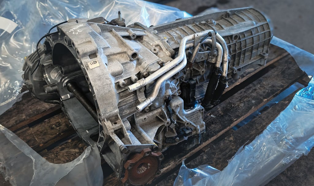 Audi A6 automatic car transmission unit sitting on a wooden pallet in an auto repair shop.