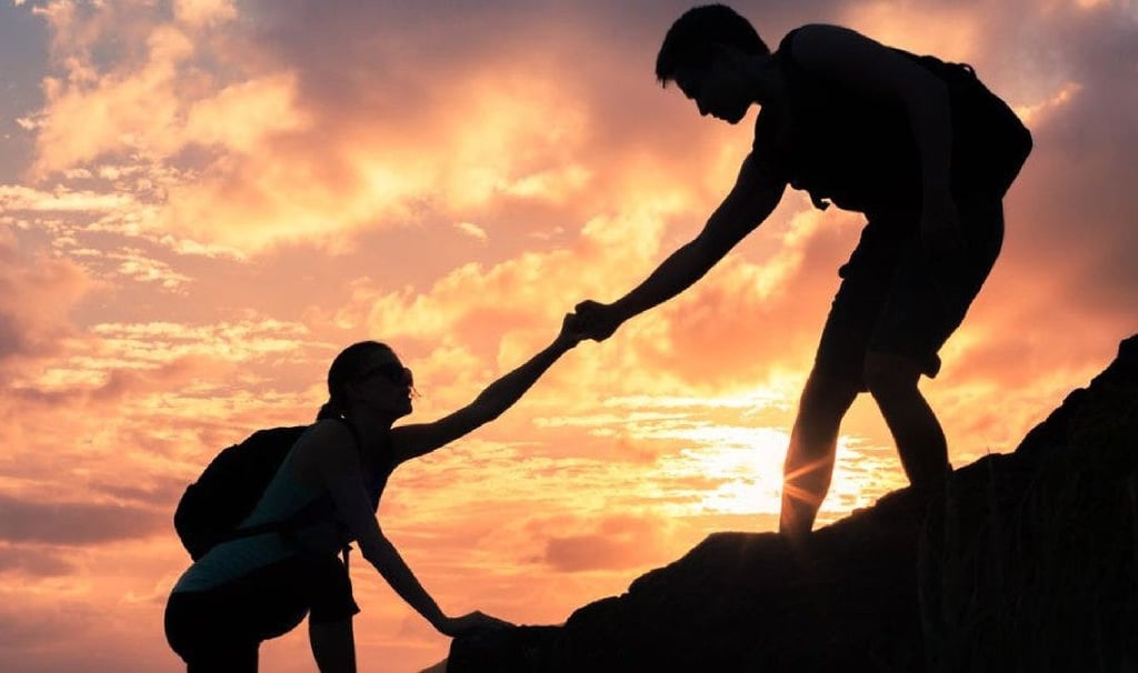 a man helping another man climb a mountain