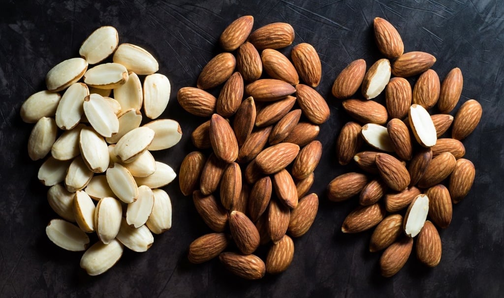 Bodegón comparativo mostrando almendra Marcona redondeada, Largueta alargada y Comuna sobre una mesa de madera - Raw Rico