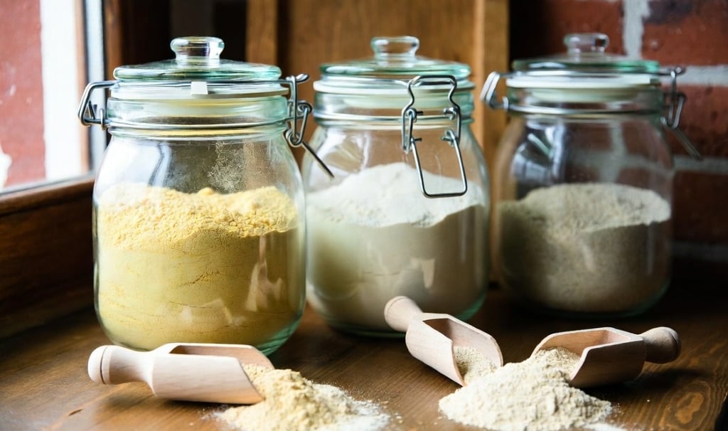 Tres tarros de cristal abiertos mostrando texturas de harina de almendra, harina de trigo sarraceno y harina de coco