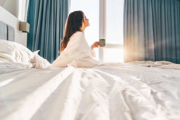 Mujer tomando café en la cama frente a la ventana