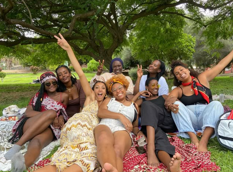 Un grupo de mujeres africanas y afrodescendientes sentadas sobre una manta en un parque