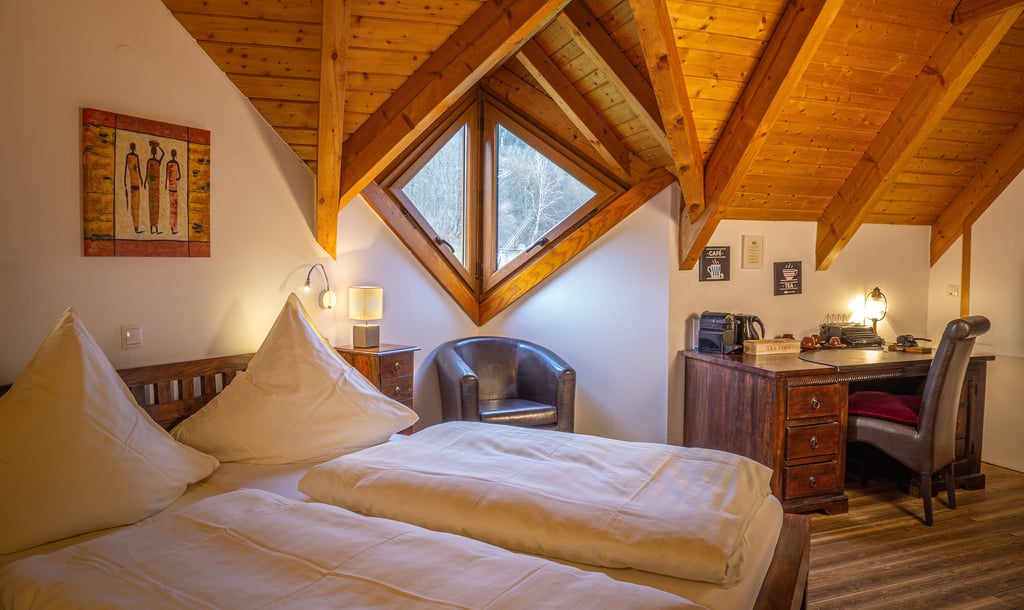 Gemütliches Dachzimmer mit Holzdecke, Doppelbett und Vintage-Schreibtisch am Fenster