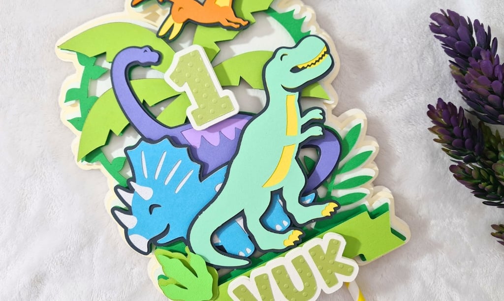 Colorful paper cake topper featuring a cartoon dinosaurs theme with the number "1" at the center. Th