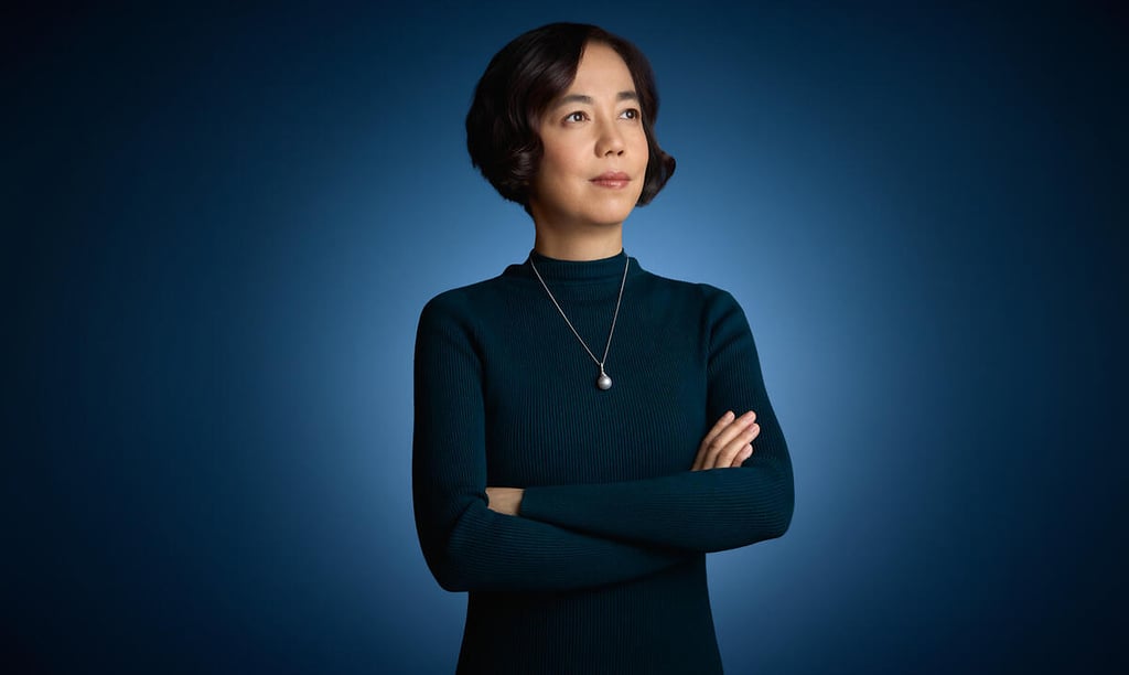 Professional portrait of a confident woman with arms crossed, wearing a dark sweater and pearl necklace.