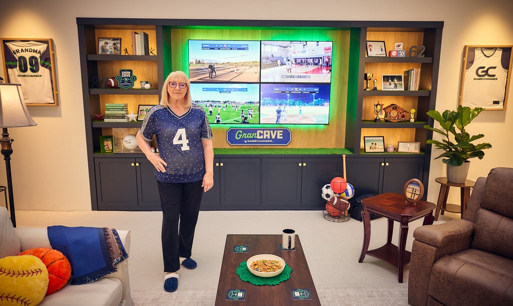 Senior woman standing in a sports-themed fan cave with multi-screen TV displaying live games.