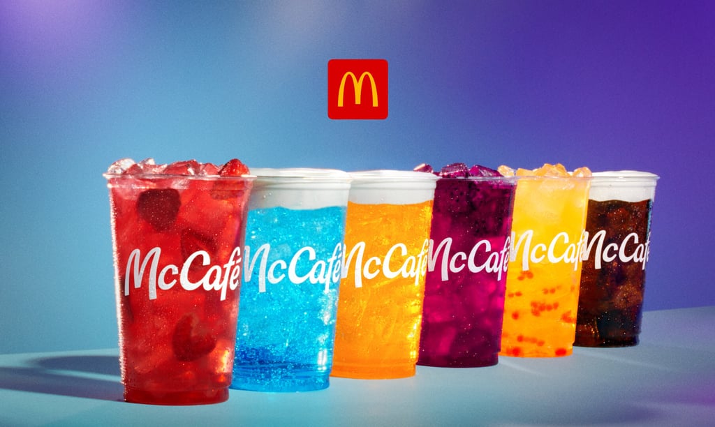 A row of colorful McCafé iced fruit drinks with foam toppings and a McDonald's logo overhead.