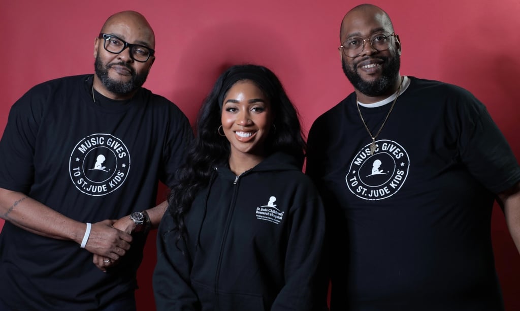 Three people smiling in black Music Gives to St. Jude Kids apparel against a red background.