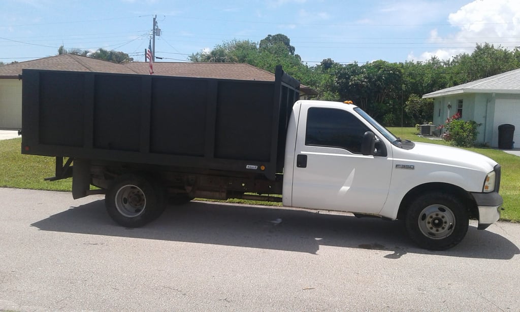 A white Ford F-350 dump truck with a black cargo bed parked on a residential street.