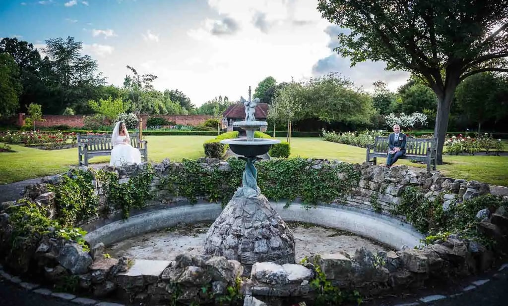 a bride and groom in a garden with a fountain