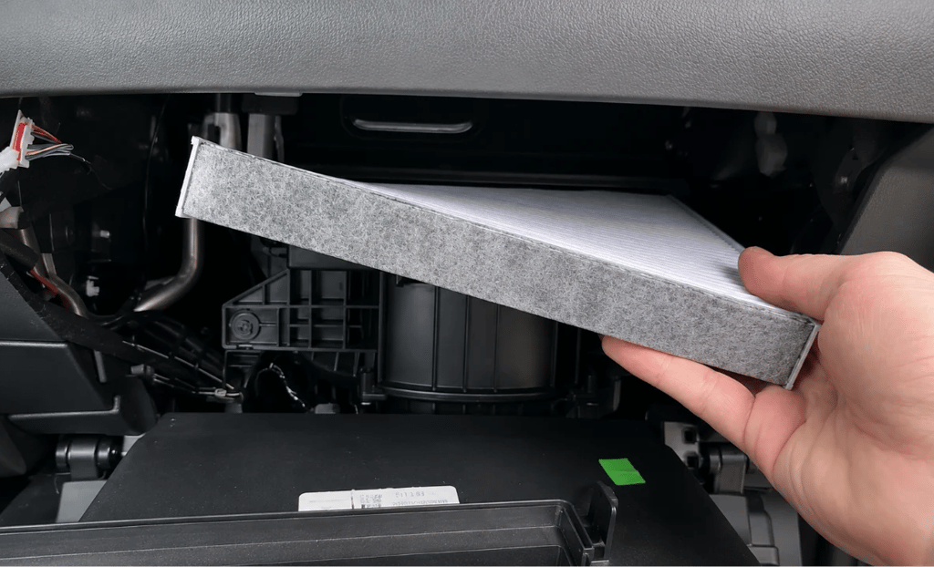Motorista removendo filtro de cabine do carro durante troca para melhorar a qualidade do ar.