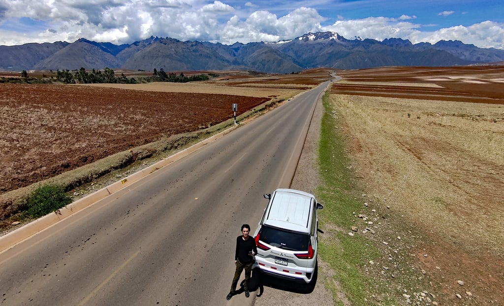 ペルーの高地を走る一本道とアンデス山脈を望む風景。道路脇に停車した車の前に立つ笹野大輔編集長