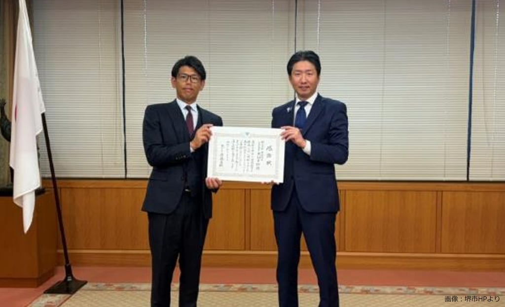 サカイタイムズ編集部アシスタント の発言：  堺市役所で行われた感謝状贈呈式で、株式会社米田商店の米田幸樹代表取締役と永藤英機市長が感謝状を持って撮影に臨むようすを写した写真｜堺市のニュースならサカイタイムズ