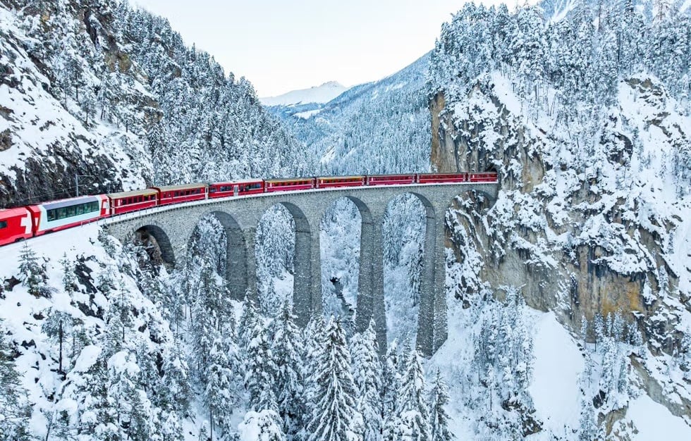 Glacier Express luxury train crossing a snowy viaduct in the Swiss Alps.