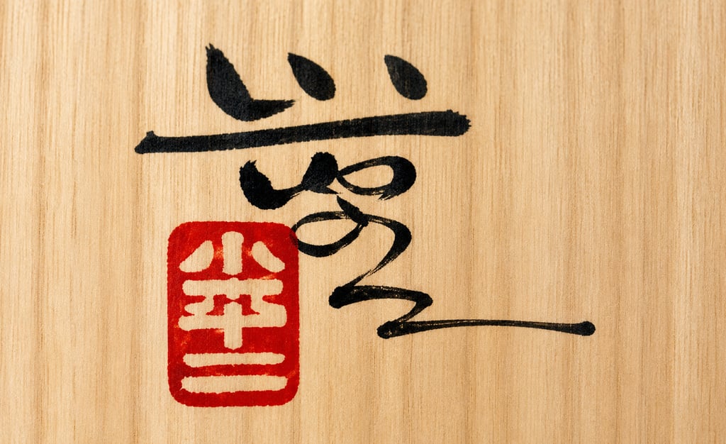 Traditional Japanese calligraphy ink characters and a red hanko seal stamp on a light wood background.