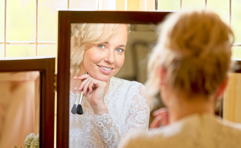 bride's reflection in the mirror looking into the camera lens with a big smile on her face